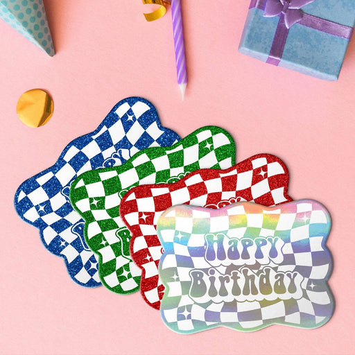 Four groovy birthday gift tags in metallic rainbow, glitter blue, glitter green, and glitter red lying beside colorful gifts and party decorations.
