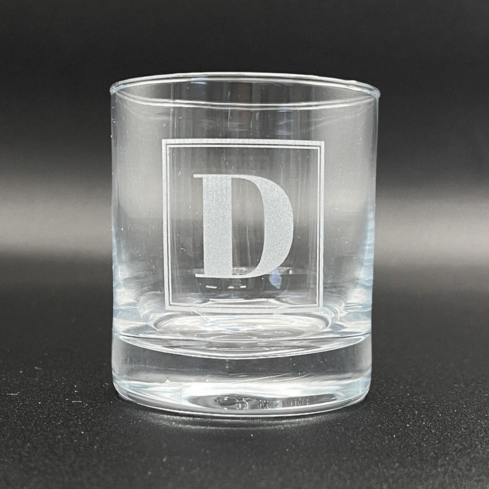 Close-up image of an empty whiskey glass with the framed initial engraving shown clearly. This view highlights the clean etching and overall glass quality.