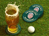 Custom square pulpboard coasters are shown sitting on a grassy, green golf course next to a pint of beer and a white golf ball. The pint of beer has a golf ball splashing into it and has a coaster underneath it. The custom coasters feature design printed with playful &quot;Swinging Into Retirement&quot; text, golf imagery, and custom photo.