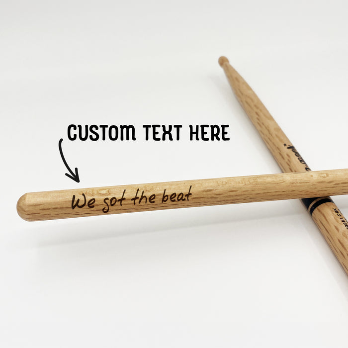 Two wooden drumsticks with custom text engraved on them, resting on a white background.