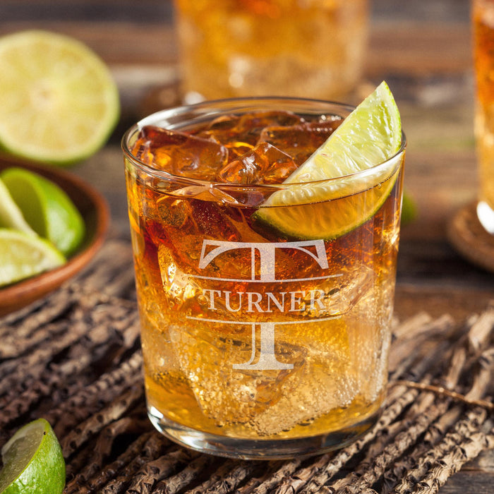Personalized whiskey glass displayed with whiskey, ice, and fresh lime on a rustic wooden surface. The bold initial and name design is clearly visible, showing how the finished custom rocks glass looks in a home bar setting.