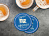 Custom round pulpboard coasters are shown sitting on a dark gray stone background with beer mugs surrounding them. The beer mugs have coasters underneath them. The custom coasters feature design printed with blue background, pink circular border, and a beige illustrated golf flag.
