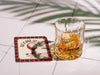 Custom square pulpboard coaster are shown laid out on marble floor. A whiskey glass is shown next to the coaster. The coaster features design with an illustration of a golf ball on a tee, checkerboard border, and custom text.