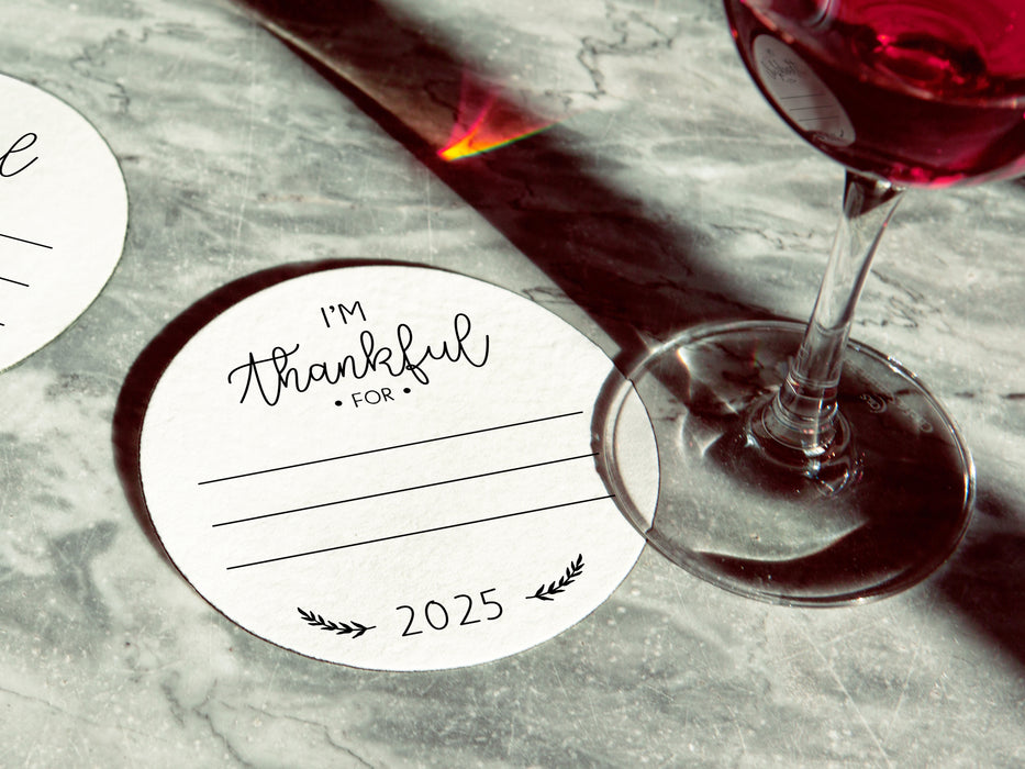 One coaster has a wine glass on it and an empty coaster sits beside it. Coasters feature the text I'm thankful for, has lines for writing in a response, and current year.
