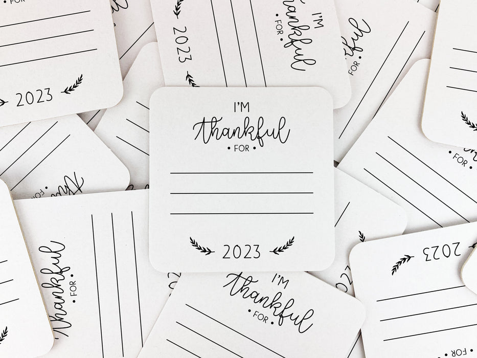 Multiple square coasters shown spread in all different directions. Coasters shows the text I'm thankful for, has lines for writing in a response, and current year.