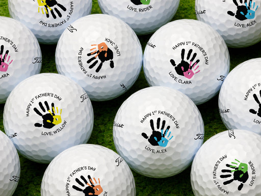 multiple white titleist golf balls with custom personalized name happy 1st fathers day handprint designs on golf course grass