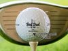 "Custom Names Here" single white titleist golf ball with customizable personalized black Best Dad By Par design on beige golf tee in front of golf club and golf course grass