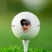 single white titles golf ball with cut out photo face on it against a grass golf course background