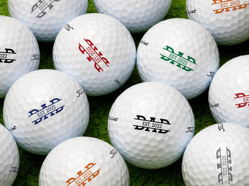 multiple white titleist golf balls with custom personalized established dad designs in different colors ontop of green grass