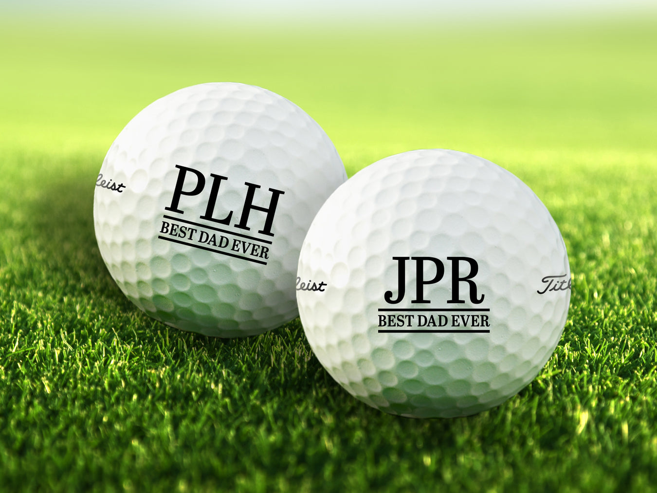 two white titleist golf balls with customizable personalized initial Best Dad Ever designs on top of golf course grass