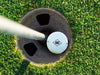 single white titleist golf ball with printed custom monogram design in golf course hole next to a pole surrounded by golf course grass