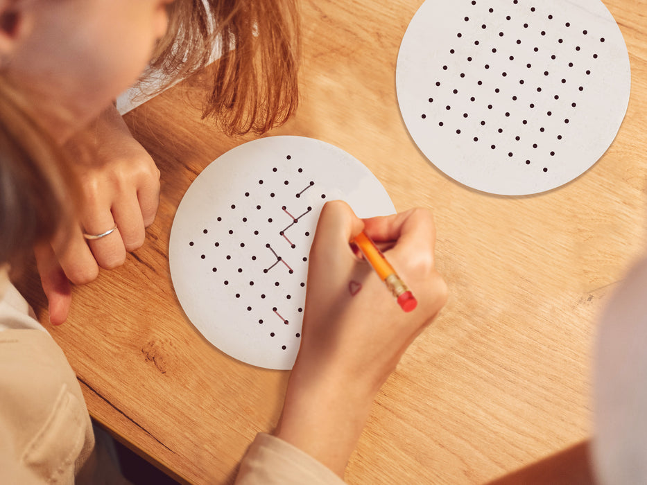 two white dots and boxes party game design on wooden table being drawn on by girl holding pencil