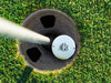 single white titleist golf ball with custom personalized black scroll monogram printed design in golf course hole next to a pole surrounded by golf course grass