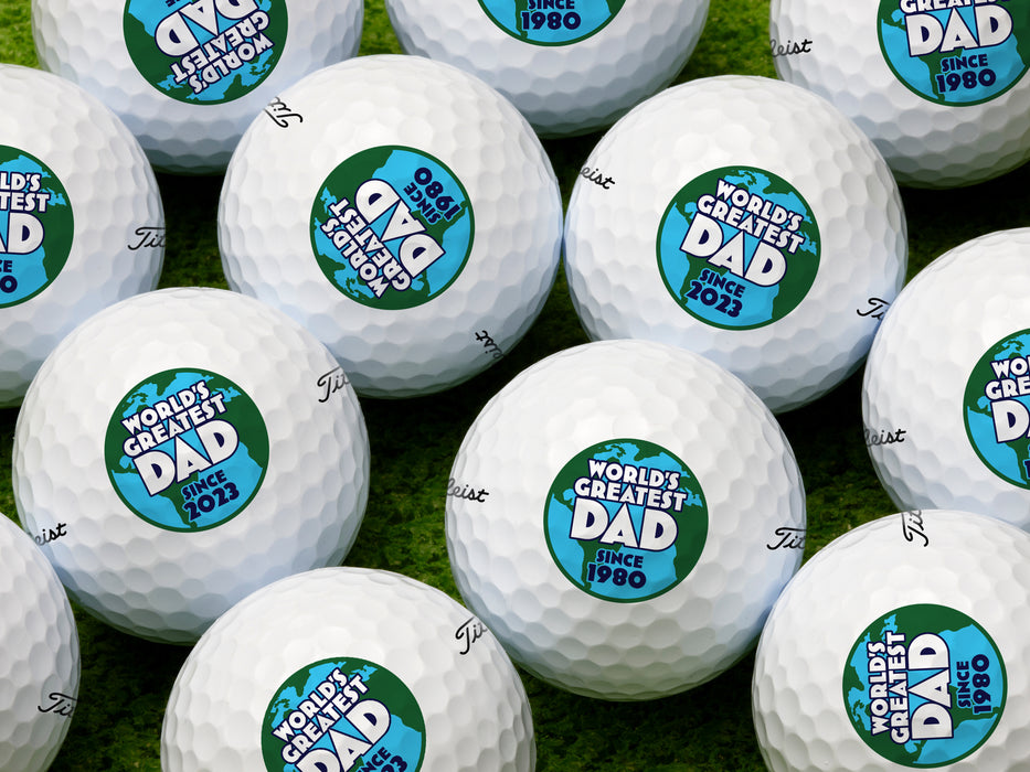 multiple white titleist golf balls with customizable personalized World's Greatest Dad Globe Graphic with year designs on top of grass
