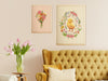 two large easter prints in gold frames on cream living room wall over yellow couch with throw pillows next to a wooden side table with pink tulips in a vase