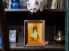 small single photo frame with orange art of black cat dressed as a ghost running with a pumpkin bucket filled with candy with sign that says only take one, photo is on shelf with white cat looking down