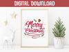 gold framed merry christmas typography print surrounded by holiday decor such as a gold hanging stars, a white deer statue, and a mini pine tree in a white plant pot