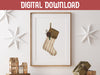 digital download: wooden frame hanging over wooden counter with christmas print of a rustic stocking surrounded by holiday decor such as white stars, mini wooden houses, and wrapped gifts
