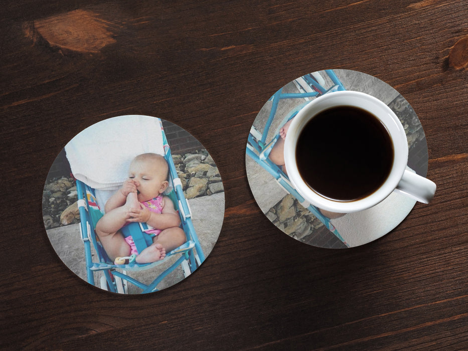 two paper photo coasters with picture of a baby on a wooden table under coffee mug