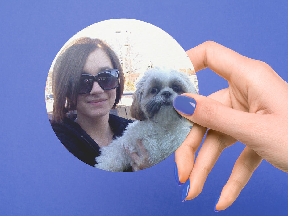single paper photo coaster with picture of a woman holding a dog being held by a hand with blue nail polish in front of a blue background