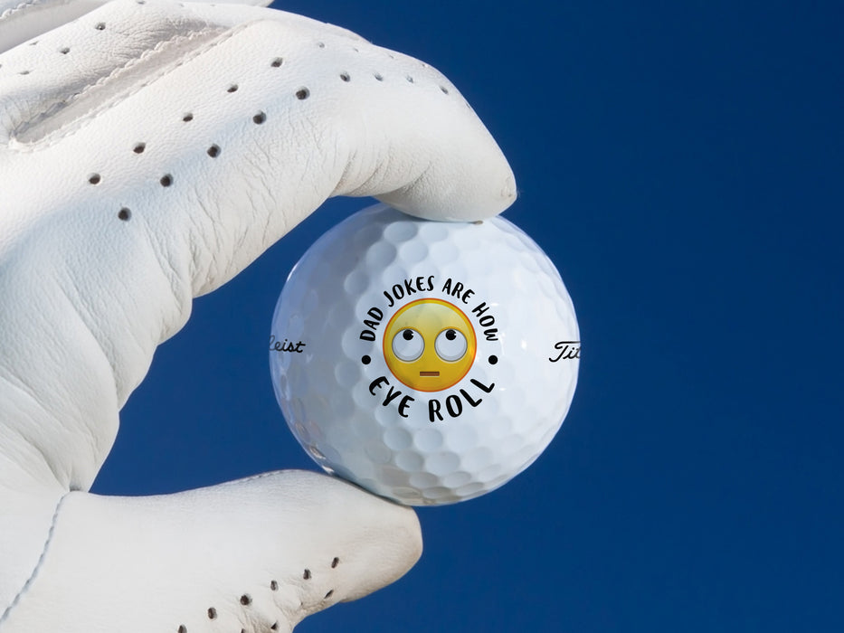 white gloved hand holding a singe white titleist golf ball with dad jokes are how eye roll emoji design in front of a dark blue background