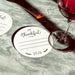A white coaster says "I'm Thankful for" and "2026" on it, placed on a marble surface next to a glass of red wine.