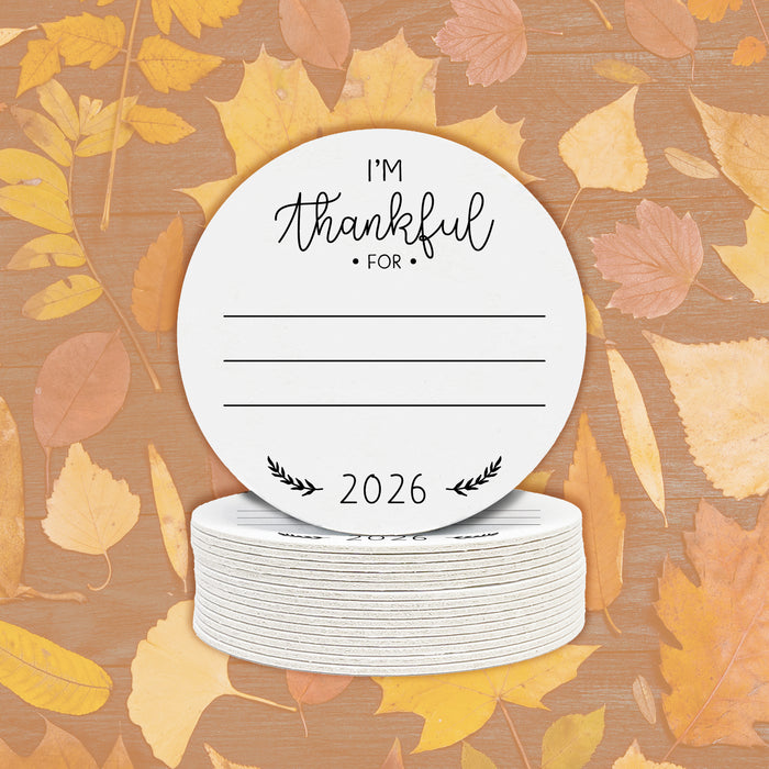 A stack of off-white round paper coasters are shown with a Thanksgiving design on them with fall leaves behind them.