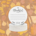 A stack of off-white round paper coasters are shown with a Thanksgiving design on them with fall leaves behind them.