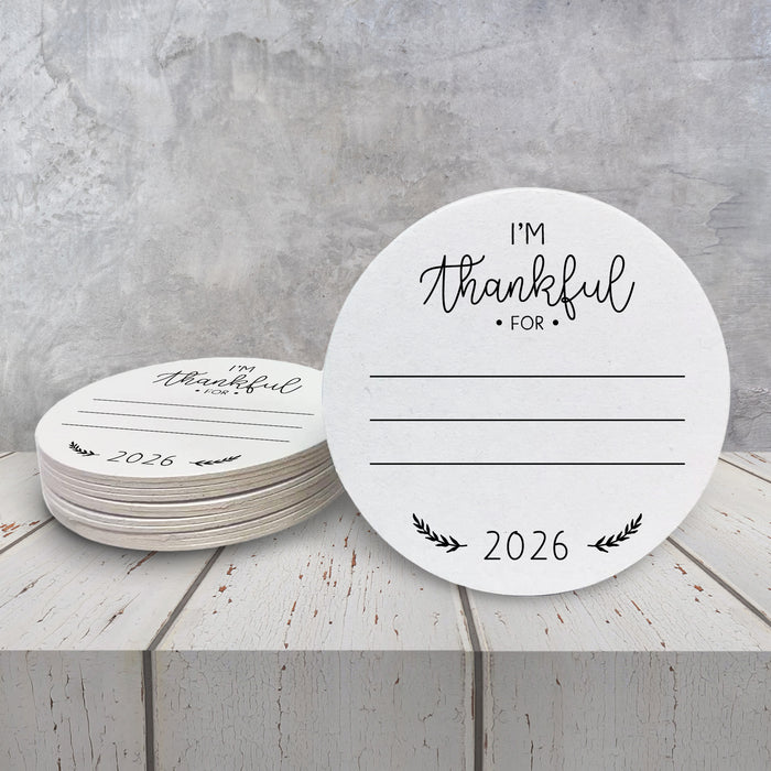 A stack of white paper coasters with the text "I'm Thankful for" and "2026" printed on them, placed on a white wooden surface.