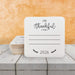 A white coaster with a message that says "I'm Thankful for" and "2026" printed on it, placed on a wooden surface. A stack of coasters with the same print are set behind the single coaster.