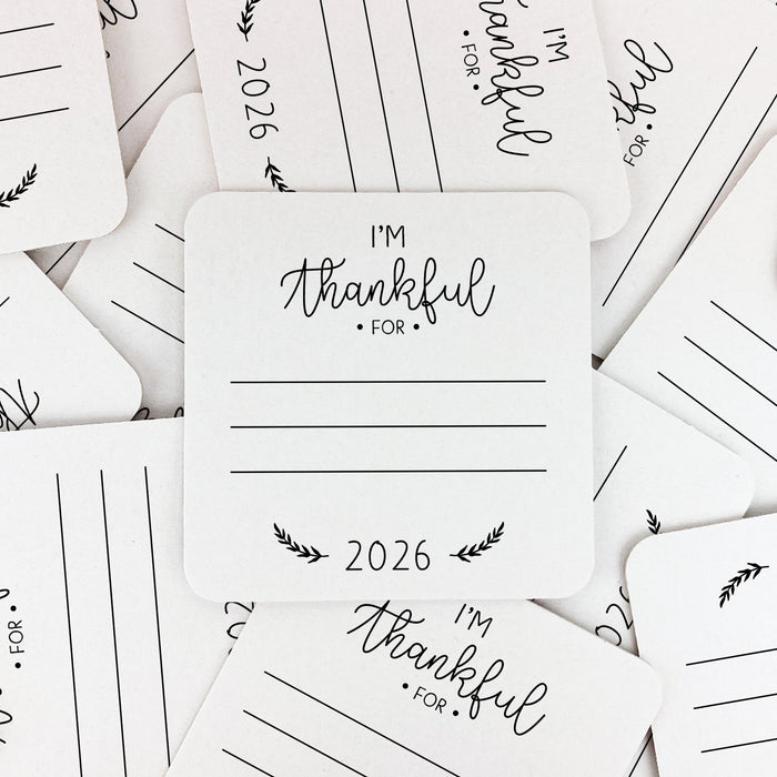 a collection of white coasters with black text and illustrations, arranged in a scattered pattern. The coasters are printed with the text "I'm Thankful for" and lines for people to write on.
