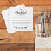 A table setting with coasters that say "I'm Thankful for" and "2026" printed on it, along with a fork and knife placed on a burlap napkin.