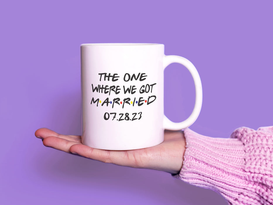 white mug on white table with friends design typography that says The One Where We Got Married 07.28.23 in front of purple background being held by a hand with a pink sweater