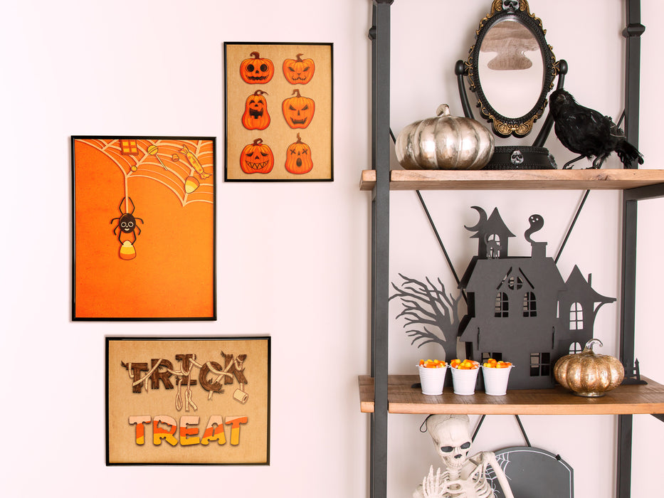 3 Frames of wall art with halloween designs on white wall next to decorative shelf with candy, skeleton, pumpkin, and crow decorations.  art designs include; a cat dressed as a ghost carrying a pumpkin, pumpkin patterns, and a candy corn spider