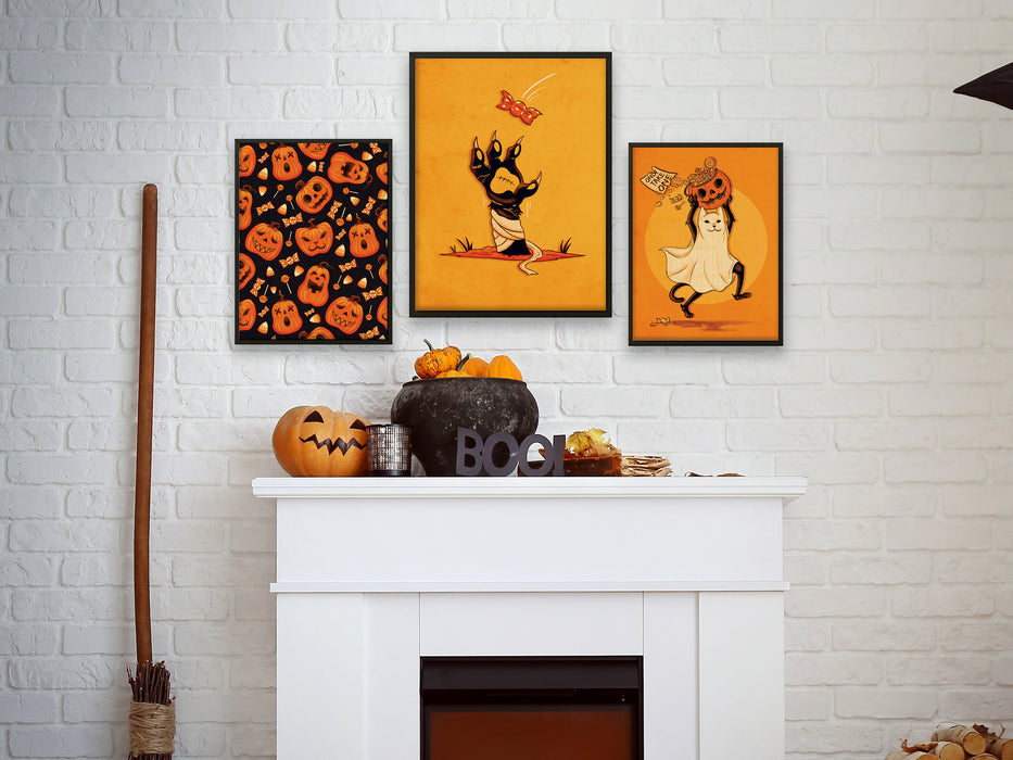 3 frames of wall art with halloween designs over a fireplace with halloween decorations like pumpkins, a boo sign, and a broomstick. Halloween designs include, pumpkin pattern, zombie cat paw, and a cat dressed up as a ghost carrying a pumpkin
