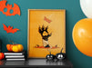 halloween zombie cat paw art print in wooden frame leaning against teal wall sitting on black dresser counter surrounded by halloween decor such as orange and white balloons, bats, pumpkins, jack-o-lanterns, and candles