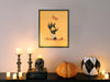 single framed poster hanging on wall with design of retro vintage halloween art of zombie mummy cat paw reaching for a piece of candy over countertop surrounded by decor such as candles, pumpkins, and a black skull ontop of books