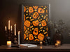 halloween pumpkin pattern art print within elegant black frame in front of black wall sitting ontop of brown counter surrounded by halloween decor such as candles, papers, potted plant, and a black skull