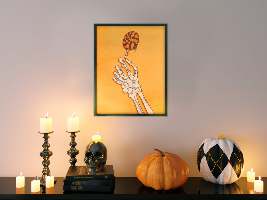 white wall with single frame of yellow art of a skeleton hand holding a lollipop with retro vintage textures and patterns, living room with couch with halloween decorations such as candles, pumpkins, and a black skull ontop of books