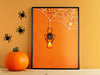 candy crazed spider print in black frame leaning against orange wall surrounded by halloween decor such as spiders and a pumpkin