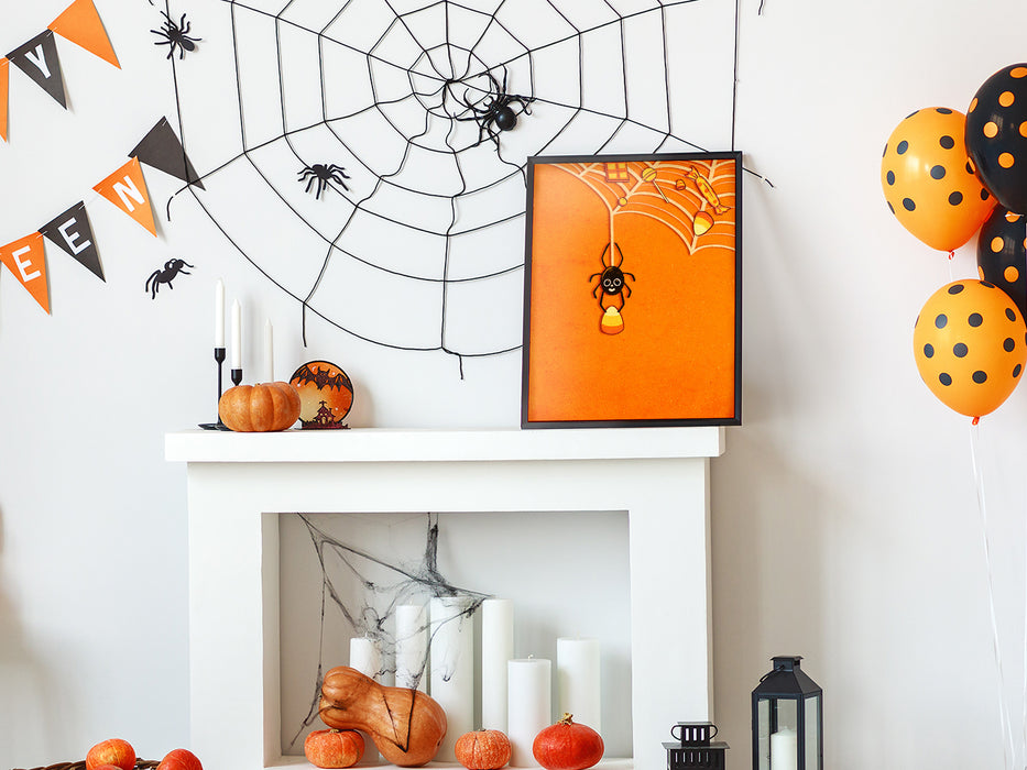 Single framed print of spider holding candy corn with web full of candy and orange background against a white wall on top of a fireplace surrounded by halloween decoration such as pumpkins, spider webs, balloons, banners, and spiders