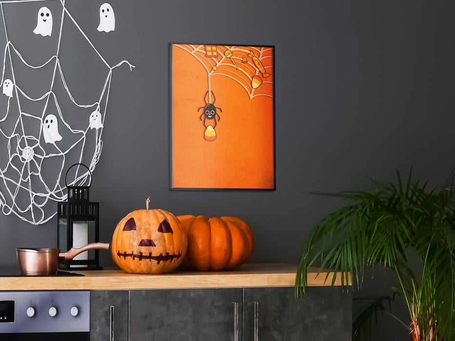 Single framed wall print of spider holding candy corn with web full of candy and orange background against a black wall over a kitchen counter surrounded by halloween decoration such as pumpkin, spider webs, ghosts,