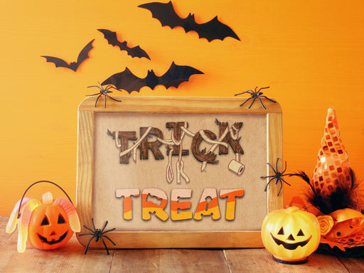 single wooden frame with halloween trick or treat typography print against orange wall surrounded by spider, jack o lanterns, witch hat decor