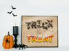 Halloween Trick or treat typography art print in black frame in front of white wall surrounded by halloween decor such as spiders, bats, pumpkins, and a candle.