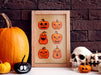 Single wooden frame of halloween art print with rows of pumpkins With different faces against a dark brown brick wall on a white countertop surrounded by pumpkins, jack o lanterns, and a skull