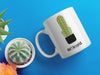 white mug with don't be a prick typography design with cactus graphic on blue background next to various potted green and orange cacti and succulents