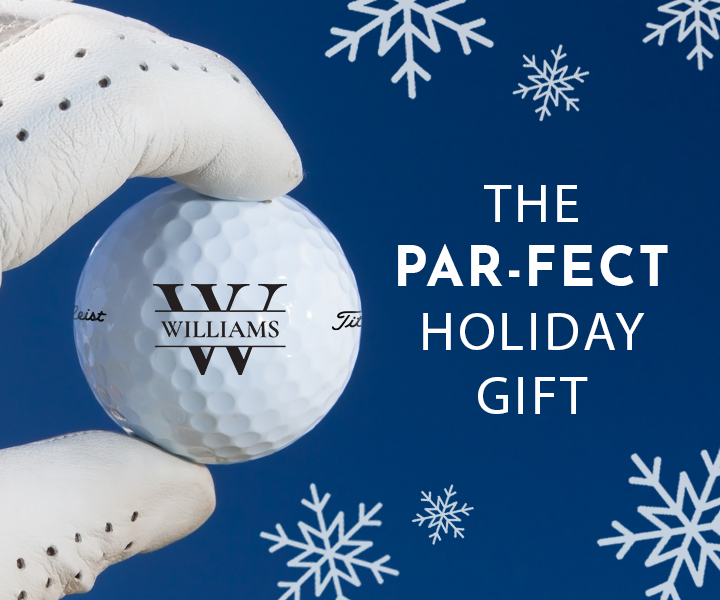 Text: The Par-Fect Gift Image: A white gloved hand is holding a custom Titleist golf ball. The golf ball has the Inital design in black with the name "Williams" printed on it. The background is blue with white snowflakes.