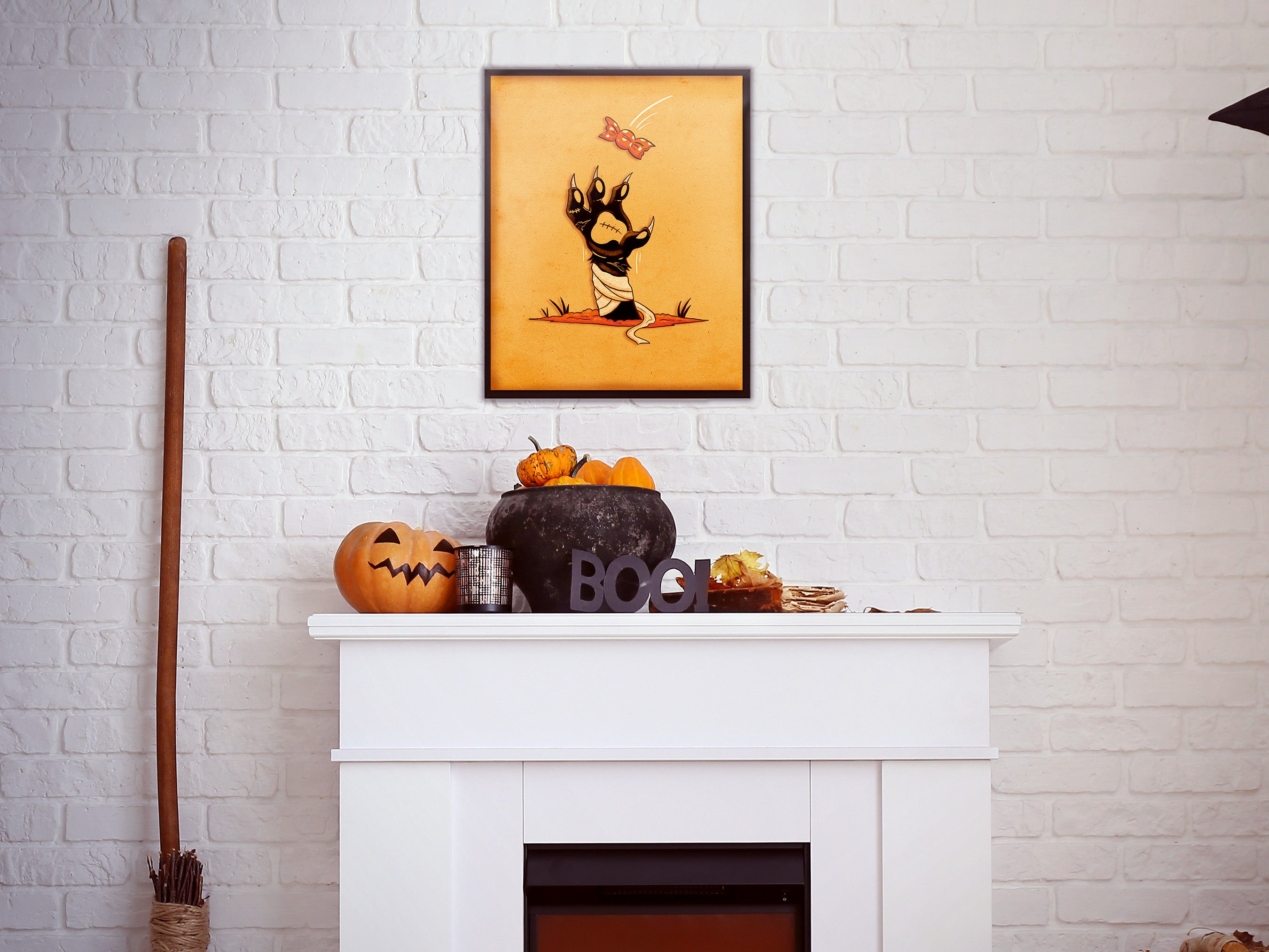 halloween zombie cat paw art print in wooden frame leaning against teal wall sitting on black dresser counter surrounded by halloween decor such as orange and white balloons, bats, pumpkins, jack-o-lanterns, and candles
