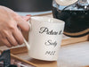 woman's hand holding white mug with golden girls inspired typography design with quote that says Picture it...Sicily 1922 pouring a pot of coffee in kitchen