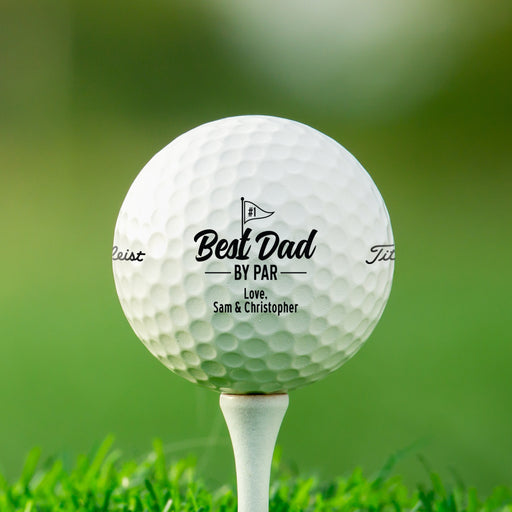 single white titleist golf ball with customizable personalized Best Dad By Par design on white golf tee in front of golf course grass background